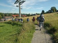Die Pfadfinderinnen der Diözese Augsburg laufen mit großen Rucksäcken hintereinander einen kleinen Weg neben einer Talstation nach oben.